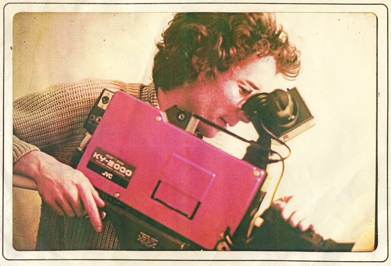 1980s, young man looking into the eyepiece of a red TV video camera.