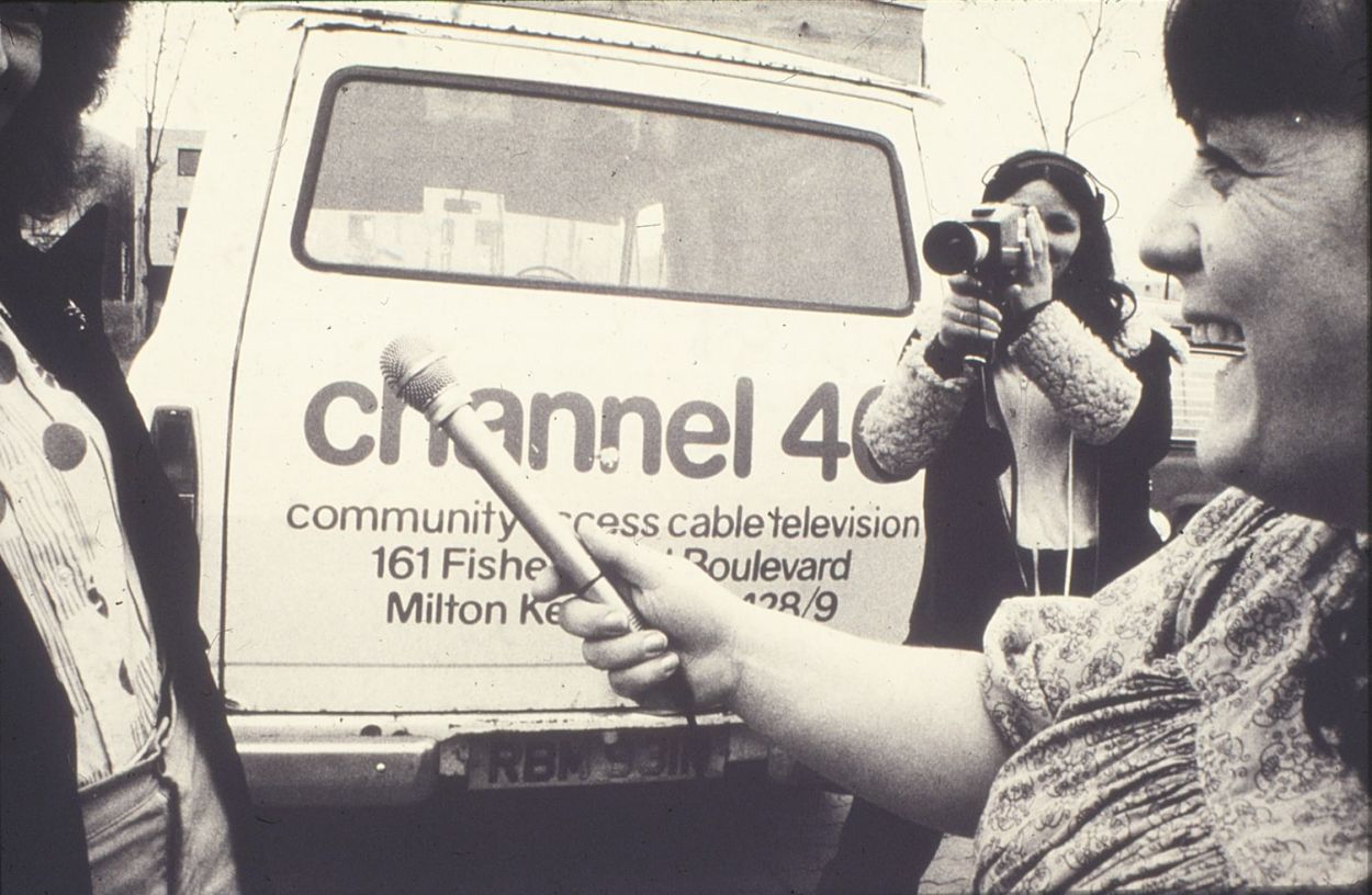 1980s photo of smiling woman with microphone, a camera woman, and a van with the text 'Channel 40 community access cable television, Milton Keynes