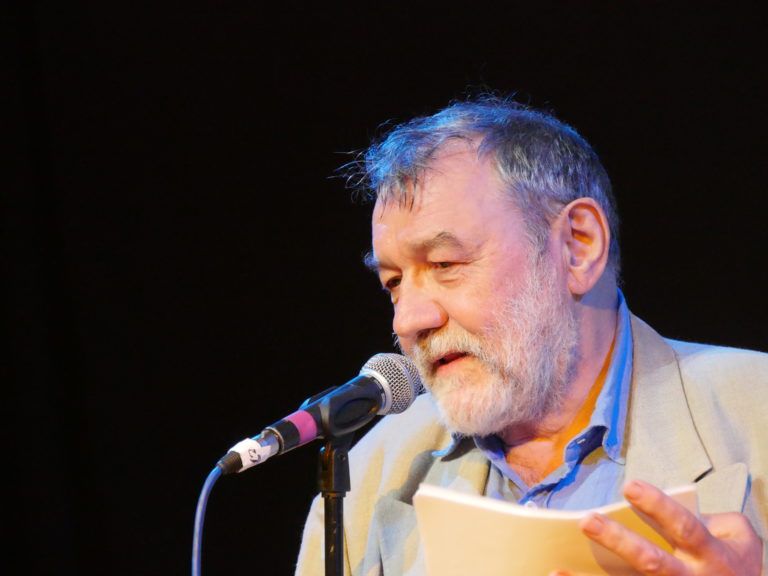 Alan Sutherland reading from a text at a microphone.